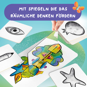 Produktbild eines Kinder-Lernspiels auf türkis-grünem Hintergrund.  Oben steht in weißer Schrift auf einem lila Balken: „Mit Spiegeln die das räumliche Denken fördern". Rechts daneben ist ein illustrierter bunter Schmetterling zu sehen.  Im Bild sind mehrere quadratische Spielkarten mit abgerundeten Ecken verteilt. Auf den Karten sind schwarz-weiße Skizzen abgebildet: ein Auge, ein Bleistift, eine Sprechblase und ein Seestern. In der Bildmitte hält eine Kinderhand einen kleinen dreieckigen Spiegel über eine große, farbenfrohe Karte mit einer fantasievollen Figur – einem bunten Mischwesen aus Fisch und Fantasiegestalt in leuchtenden Regenbogenfarben. Der Spiegel zeigt, wie durch seine Reflexion ein vollständiges, symmetrisches Bild entsteht.