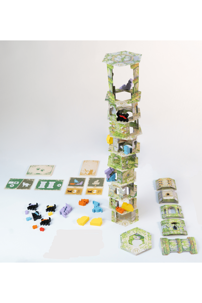 Produktfoto auf weißem Hintergrund. Im Zentrum ein aufgebauter, hoher Papierturm aus ca. 10 übereinandergestapelten, leicht versetzten Stockwerken mit grünem Rankenmuster. In verschiedenen Etagen sitzen bunte Katzenfiguren (schwarz, lila, blau, gelb, orange). Links vor dem Turm liegen mehrere kleine Katzenfiguren in verschiedenen Farben sowie Spielkarten in Grün und Beige. Rechts liegen noch nicht aufgebaute Wandplättchen und Turmteile. Vor dem Turm steht ein sechseckiges Bodenplättchen mit der Nummer 11.