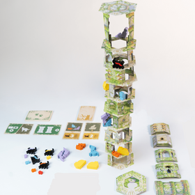 Produktfoto auf weißem Hintergrund. Im Zentrum ein aufgebauter, hoher Papierturm aus ca. 10 übereinandergestapelten, leicht versetzten Stockwerken mit grünem Rankenmuster. In verschiedenen Etagen sitzen bunte Katzenfiguren (schwarz, lila, blau, gelb, orange). Links vor dem Turm liegen mehrere kleine Katzenfiguren in verschiedenen Farben sowie Spielkarten in Grün und Beige. Rechts liegen noch nicht aufgebaute Wandplättchen und Turmteile. Vor dem Turm steht ein sechseckiges Bodenplättchen mit der Nummer 11.