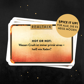 Quadratische Grafik mit schwarzem Hintergrund und goldenen Glitzerpunkten. Zentral ein Stapel Spielkarten mit flammenrotem Farbverlauf (gelb zu rot). Die oberste Karte zeigt das „REALTALK"-Label in Gold und die Frage: „HOT OR NOT: Wessen Crush ist immer primär eines – heiß wie Xaden?" Oben rechts ein goldener Kreis-Sticker mit dem Text: „SPICE IT UP! FÜR ALLE, DIE ES HEISS MÖGEN".